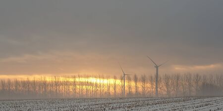 Snowy landscape at sunrise or sunset with windmilsの写真素材