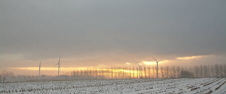Snowy landscape at sunrise or sunset with windmilsの写真素材