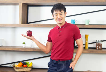 Healthy lifestyle and freshness concept. Smart, young and healthy Asian man showing apple smiling and looking at camera.の写真素材