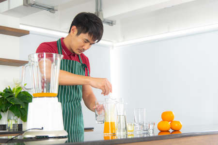 Portrait smart and handsome Asian man preparing healthy meal and fresh organic orange juice in the loft style kitchen.の写真素材