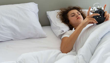 Beautiful woman on white bedding wake up when clock alarm in the morning.
