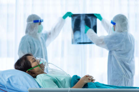 Aging woman patient infected  on bed and two medical staffs is checking patient x-ray film in ICU...