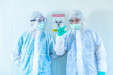 Two ASIAN medical staffs wear PPE suit and medical gloves showing COVID-19 vaccine in quarantine roomの写真素材