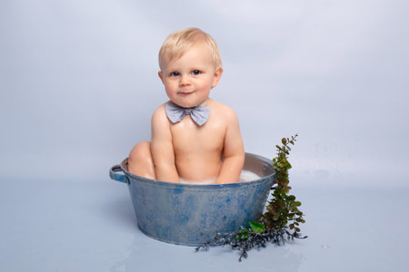 a cute boy on a blue background bathes in a blue basin. happy child playing with water. child offended turned back the concept of loneliness.の写真素材
