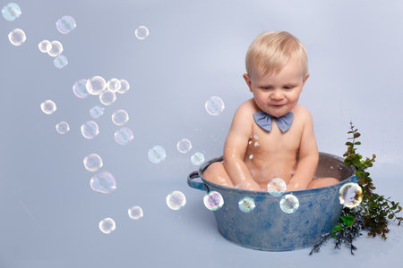 a cute boy on a blue background bathes in a blue basin. happy child playing with water. child offended turned back the concept of loneliness.の写真素材