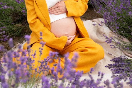 pregnant woman in a beautiful orange suit hugging her belly in a field with lavender. pregnancy conceptの写真素材