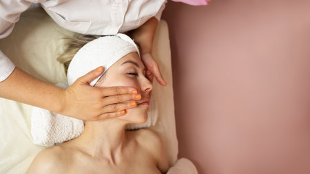 Top view of cosmetologist do facial mask for healthy glowing skin for smiling female client. Dermatologist make beauty procedures for woman patient in aesthetic medical clinic. Cosmetology concept.の写真素材