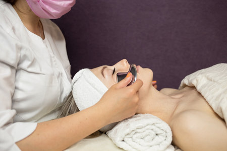 Top view of cosmetologist do facial mask for healthy glowing skin for smiling female client. Dermatologist make beauty procedures for woman patient in aesthetic medical clinic. Cosmetology concept.の写真素材