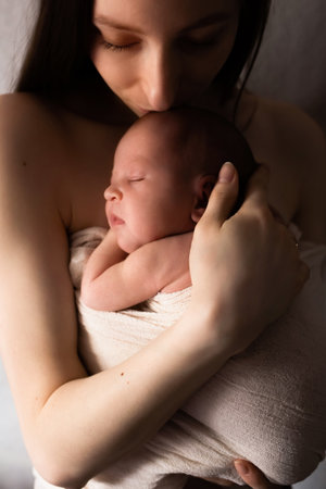 gentle close-up portrait of a mother with a newborn baby in her arms. photograph in a dark key, dark color. a happy family.の写真素材