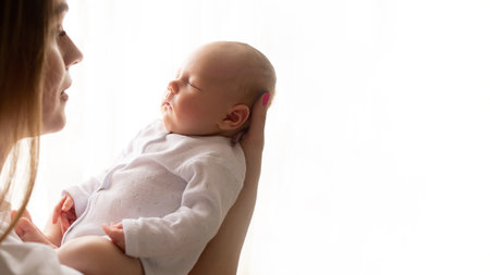mother holds the baby in her arms and carefully looks at the child against the background of the window. white background. copyspace.の写真素材