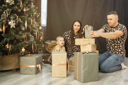 a young family with a small child unwraps gifts near the Christmas tree. family in the living room wrapping gifts for Christmas and New Yearの写真素材