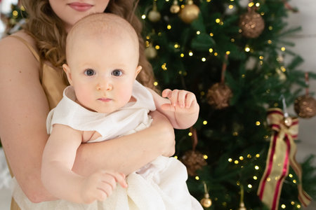 close-up portrait of a little girl in a beautiful white dress in her mother's arms against the background of a Christmas tree.の写真素材