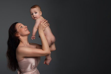 a beautiful young woman with long dark hair in a light dress holds a little boy in her arms. happy mother hugging her son on a dark background with space for text.の写真素材