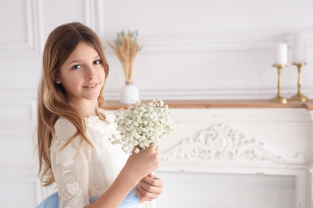 A young girl is celebrating her first communion, dressed in white with a blue ribbon, holding a bouquet of flowers. The elegant church setting adds to the special occasion.の写真素材