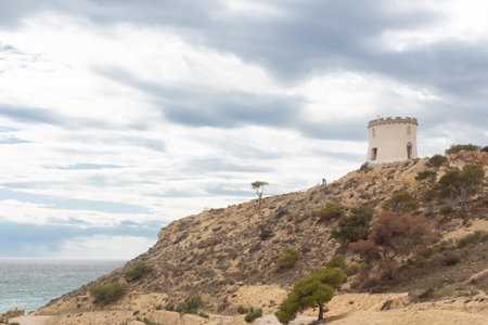 Visitors enjoy breathtaking views of the coastline and historic towers in Spain. The rocky cliffs and serene waters create a picturesque setting perfect for exploration.の写真素材