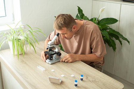 A man focuses on studying biology in his home, using a microscope to investigate plant samples. This...