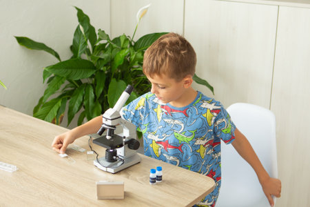 Young boy explores biology by examining plant slides through a microscope at home. He is engaged in...