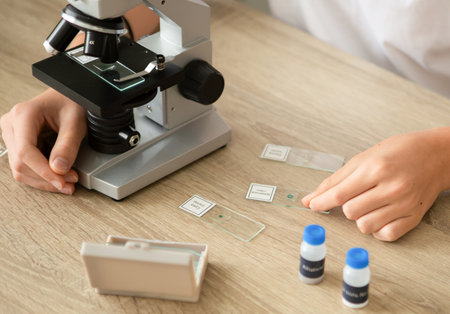 At home, a woman with long hair is focused on her biology studies. She examines plant samples using a microscope, showing the process of online learning in a calm environment.の写真素材