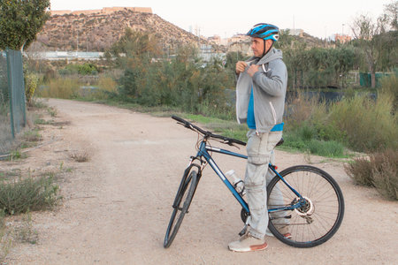 Cyclist in helmet and blue jacket standing with his bike on the road