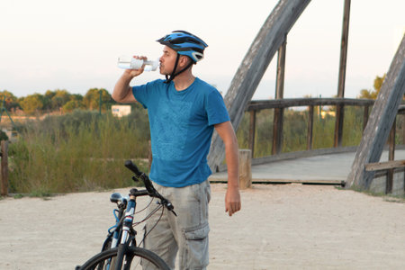 Young man drinking water from a bottle while standing with his bicycle.の写真素材