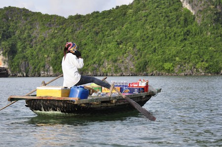 Unidentified woman talks in her mobil phone while rowing her boat on July 1, 2010 at Halong Bay, Vietnam. Mobile coverage is obviously good also far away from land.のeditorial素材