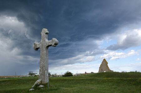Historic cross and chapel ruin in stormy weatherの写真素材