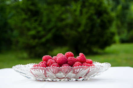 Fresh raspberries in a glass bowl on a table with green background