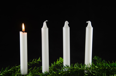Four advent candles with one of them burning at a black backgroundの写真素材