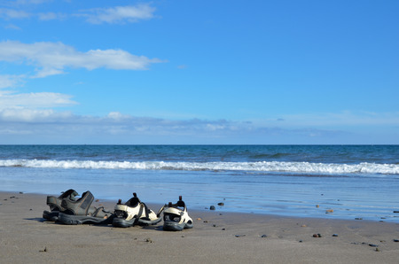 Two pair of sandals at a sand beach with waves and blue waterの写真素材
