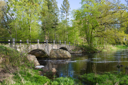 Ancient bridge over streaming water in a small river in a fresh springtime landscape. From the swedish province Smaland.の写真素材