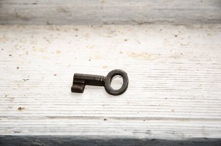 An old rusty key at a dirty white painted wooden surfaceの写真素材