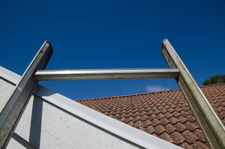 Top of a ladder at a tiled roof by blue sky