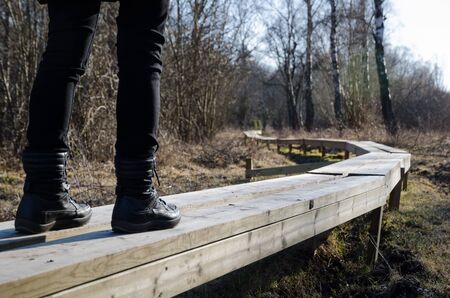 Legs with boots walks at a newly made wooden footpath in the nature