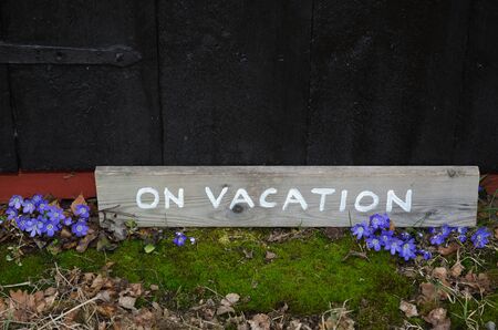 Wooden on vacation sign on the ground with blue spring flowers and green mossの写真素材