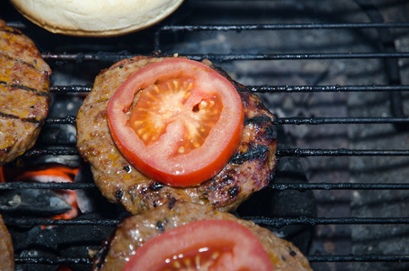 Barbequing hamburgers with tomatoes on a charcoal grillの写真素材