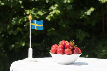 Swedish miniature flag and a bowl with fresh strawberries on a garden tableの写真素材