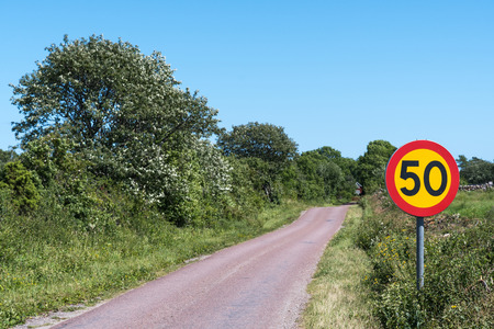 Speed limit traffic sign by a narrow road at the countryside