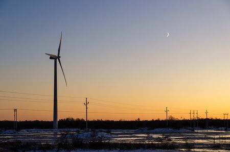 Windmill and power lines by sunset in a plain landscape by winter season