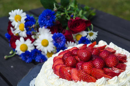 Strawberry cream cake with summer flowers on a tableの写真素材