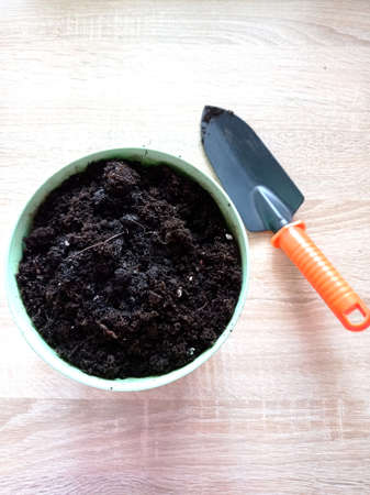 A pot with soil and a spatula nearby, tools for plant transplanting, planting plants, flowers. Metal shovel with orange handle. View from aboveの写真素材
