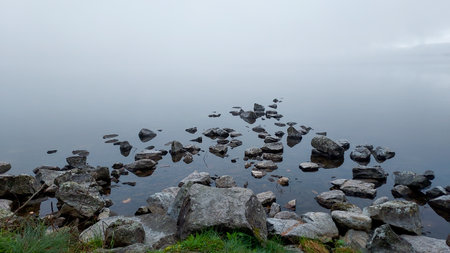Stones on the shore of a foggy lake in the morningの写真素材