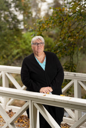Portrait of a senior woman standing on a bridge in autumn parkのeditorial素材