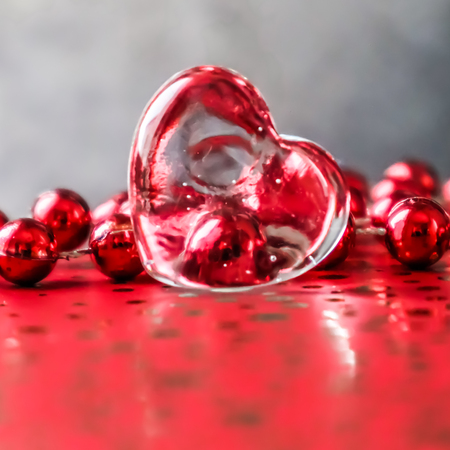 Shining transparent heart and a group of red beads. Perfect Valentine's Day greeting card background. Image in red tone on grey background in a 1x1 formatの写真素材
