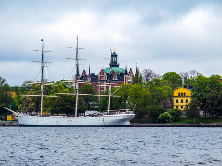 White sailboat on the background of green trees and beautiful buildings of Stockholm Swedenのeditorial素材