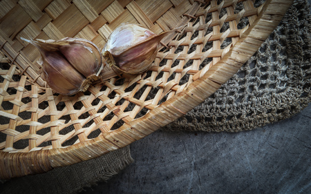 Top view of garlic cloves in a straw basket on a natural linen napkins and a rustic wooden backgroundの写真素材
