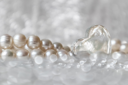 Natural white pearl beads and a transparent heart on a sparkling backgroundの写真素材