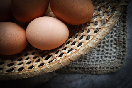 Top view of eggs in a straw basket on a natural linen napkins and a rustic wooden backgroundの写真素材