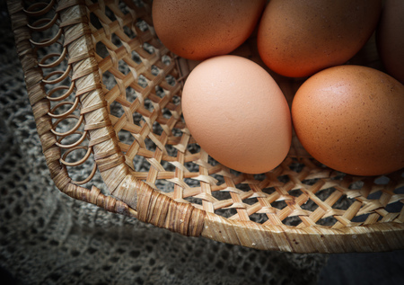 Top view of eggs in a straw basket on a natural linen napkins and a rustic wooden backgroundの写真素材
