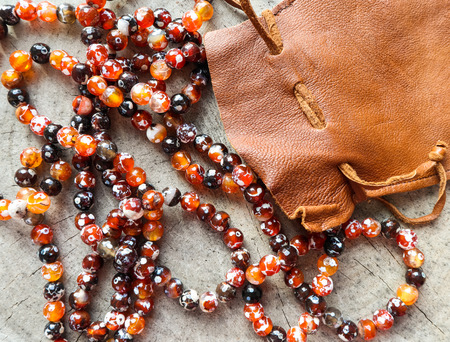 Sunny beads of amber fireplace faceted agate with leather jewelry pouch bag on rustic backgroundの写真素材