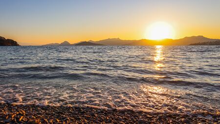 Beautiful sunset on the Mediterranean coast with islands and mountains. Stones on the beach lit by sunlightの写真素材